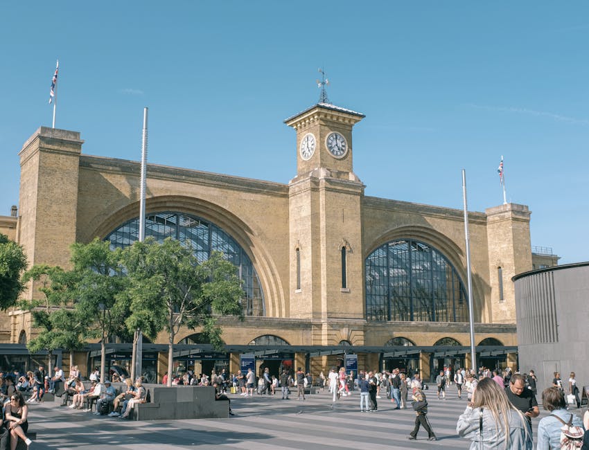 A woman standing in front of Hanwell station, part of the Elizabeth Line, with a modern brick building featuring large windows and a black canopy above the entrance. Several bicycles are parked on the